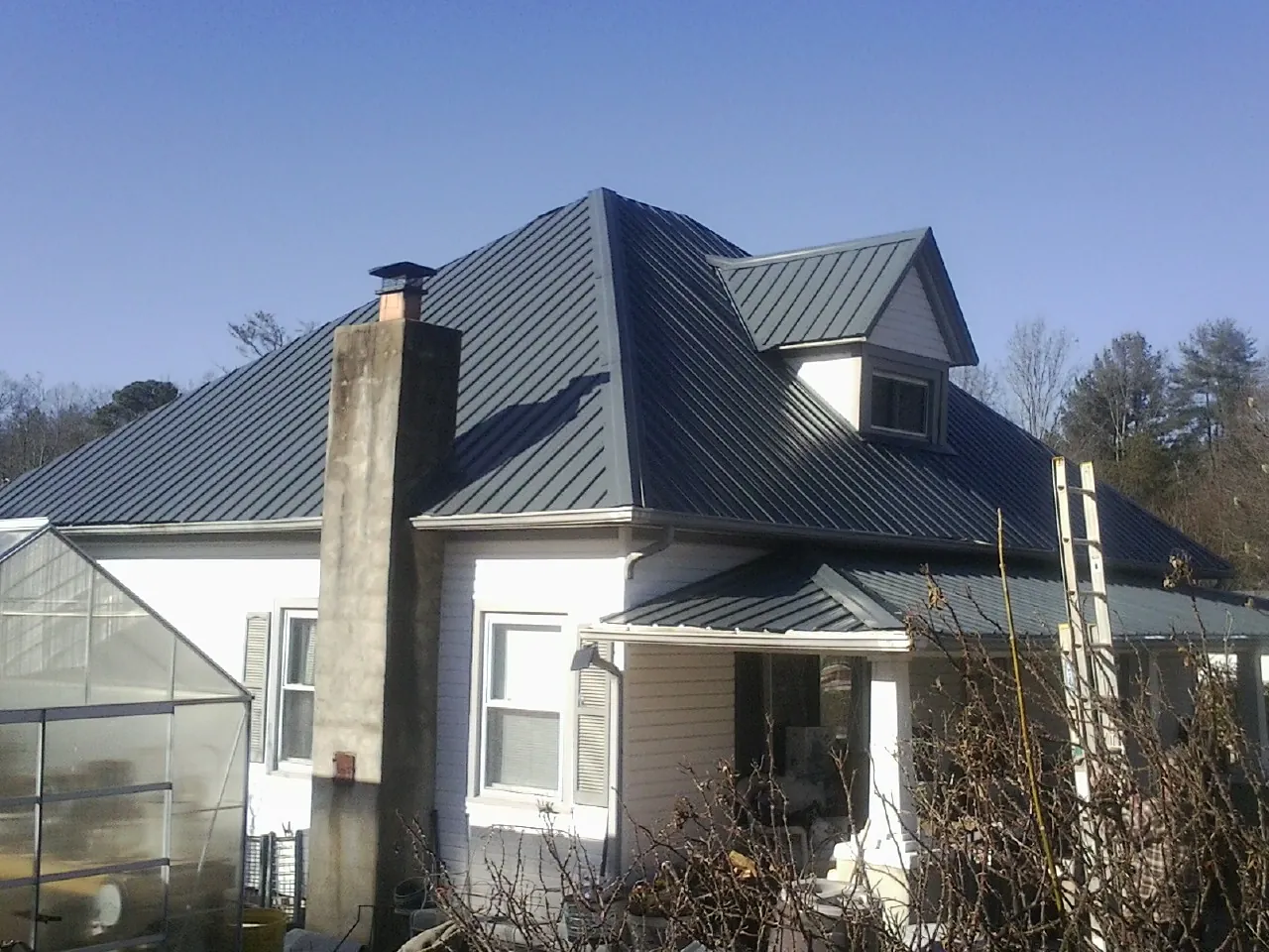 Dark blue standing seam metal roof on a white farmhouse with dormer — Slate & Tile Roof Repair by Roofing Brothers in Deltaville