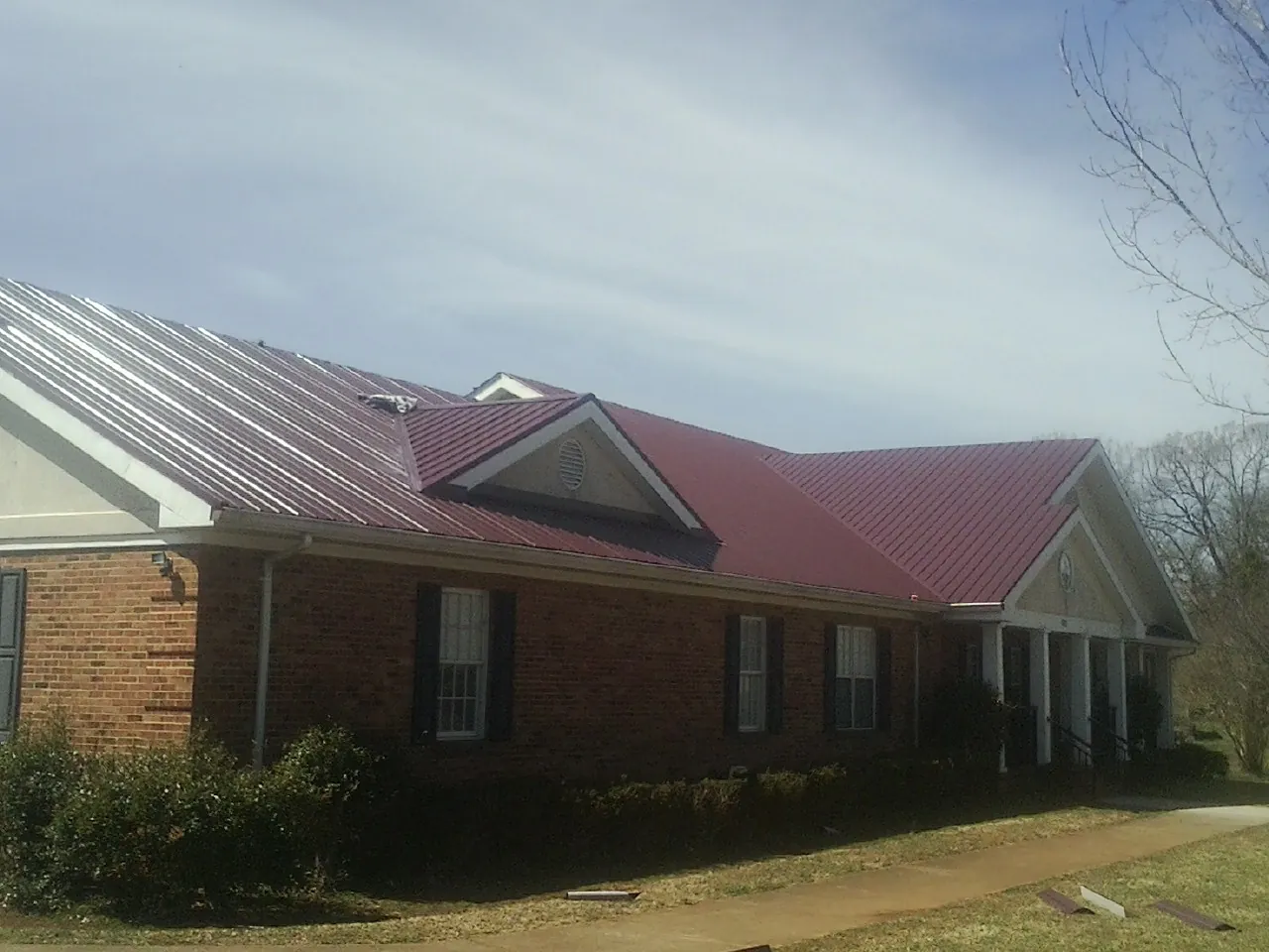 Red metal roof with gabled entries on a long brick building, from a Hail Damage Roof Repair job in Deltaville