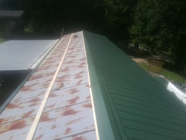 Old rusted panels beside newly installed green metal roofing — Wind Damage Roof Repair by Roofing Brothers in Deltaville
