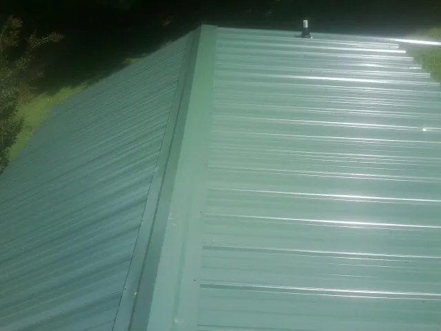 New green metal panels meeting at the ridge of a roof — Flat Roof Repair work by our crew in Deltaville