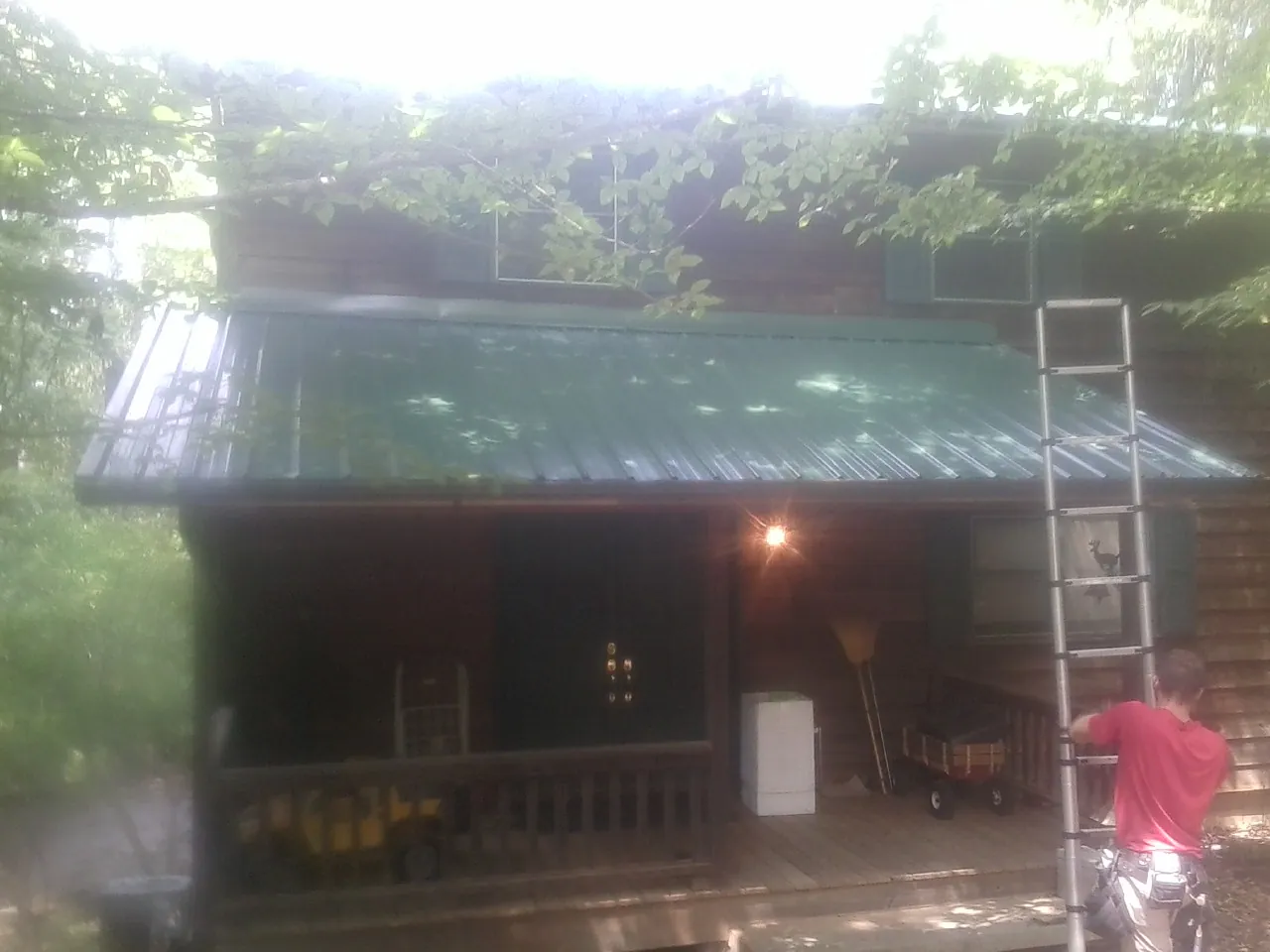 Worker on a ladder at the green porch roof of a wooded cabin in Deltaville