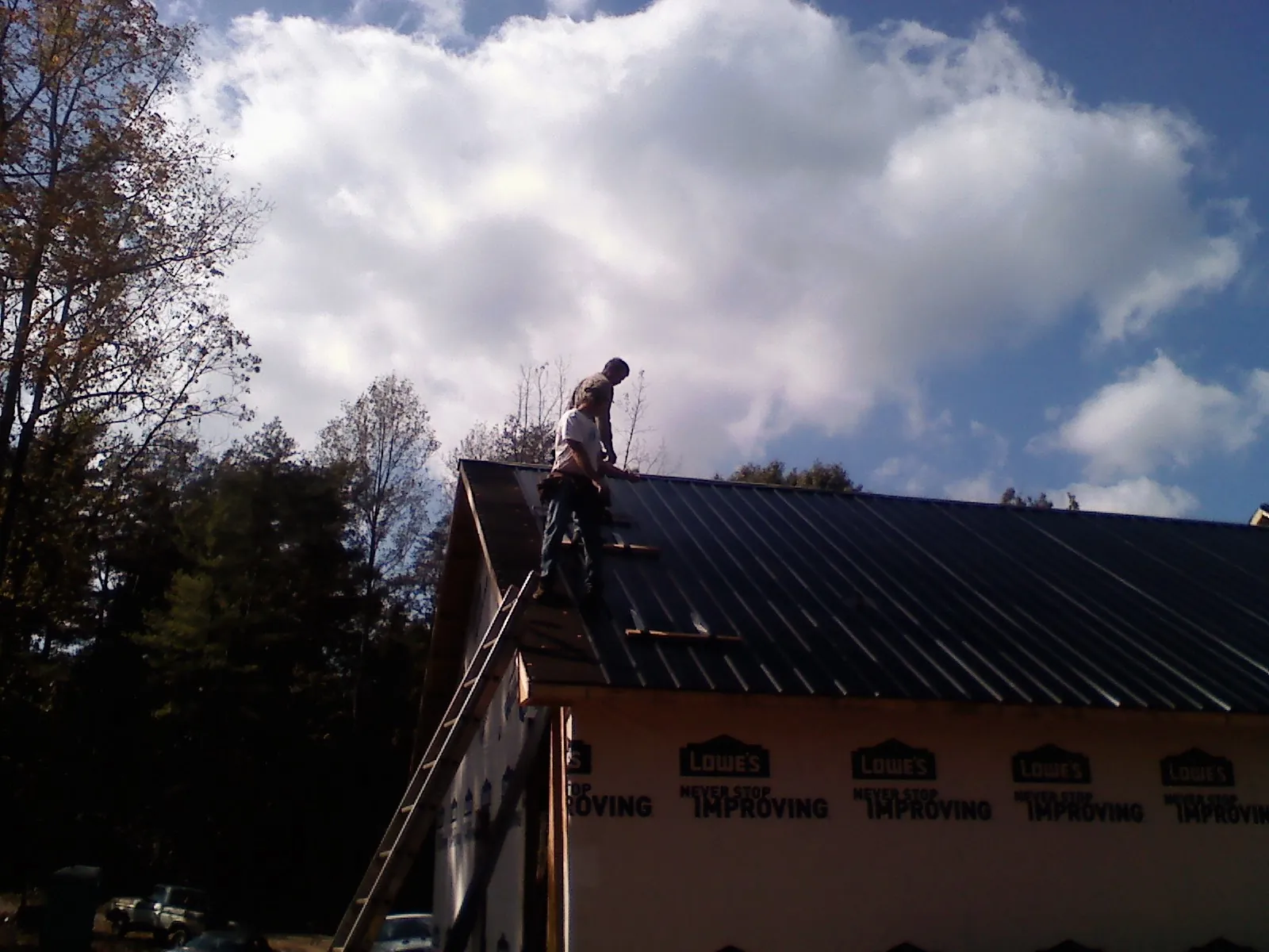 Roofer fastening dark metal panels high against a cloudy sky, from a Roof Inspection job in Deltaville